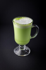 Matcha latte in a glass cup on black background.