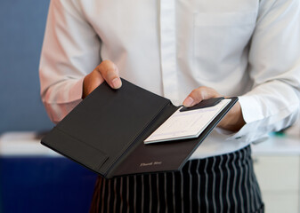 The waiter in a white shirt and apron presents a receipt after calling the bill.