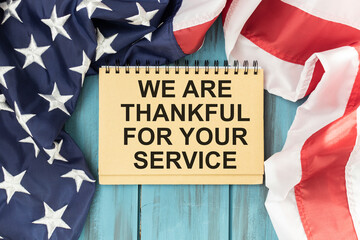 Fototapeta na wymiar WE ARE THANKFUL FOR YOUR SERVICE text on notepad and American flag.