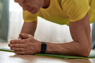 In good shape at any age. Cropped shot of a mature man fitness instructor in sportswear standing in a plank on yoga mat while exercising at home