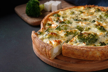 Sliced traditional french open quiche pie with feta cheese and broccoli on a dark green background. Copy space, horizontal orientation.