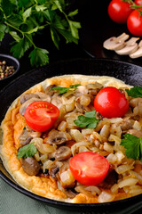 Frying pan and fresh homemade omelet with fried onions, mushrooms, cherry tomatoes and parsley.