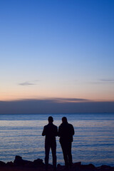 The silhouette of two young men standing on the cliff and taking photos for sunset  