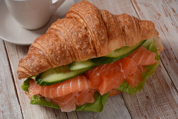 Crispy croissant with salmon and lettuce and cucumbers. Tasty breakfast.