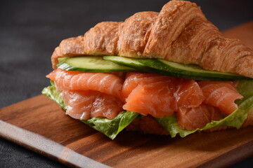 Crispy croissant with salmon and lettuce and cucumbers. Tasty breakfast.