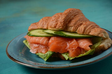 Crispy croissant with salmon and lettuce and cucumbers. Tasty breakfast.