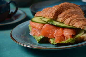 Crispy croissant with salmon and lettuce and cucumbers. Tasty breakfast.