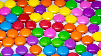 Selective focus of an array of colorful chocolate buttons on a white background. 
