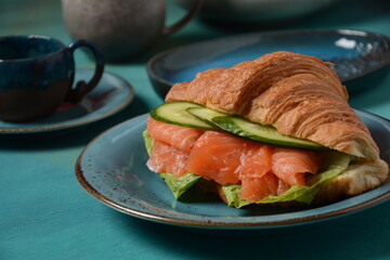Crispy croissant with salmon and lettuce and cucumbers. Tasty breakfast.