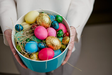 Easter celebrating. Colourful eggs in vase in female hands, close up. Festive congratulating card, christian tradition