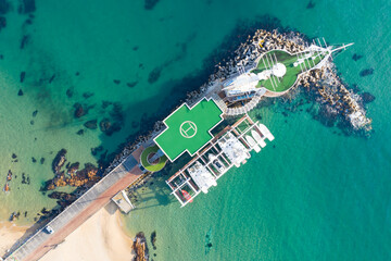 A drone photo of a small marina and the blue sea with waves.
