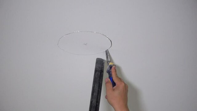 Hand with handsaw sawing hole in plasterboard ceiling
