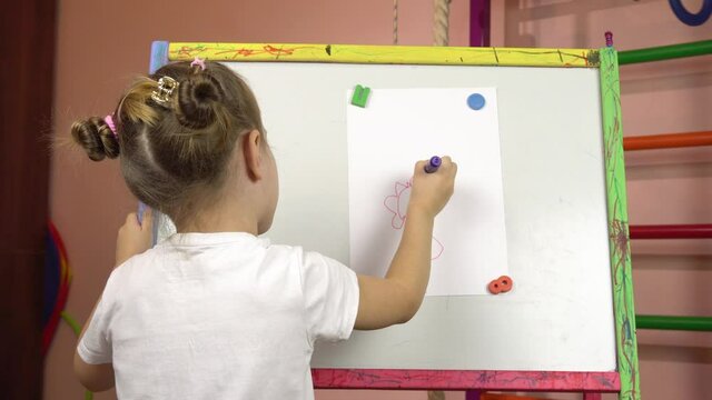 Children's creativity, early development.A little girl of five years old draws a flower with felt-tip pens on a sheet of paper on an easel.Children's room.