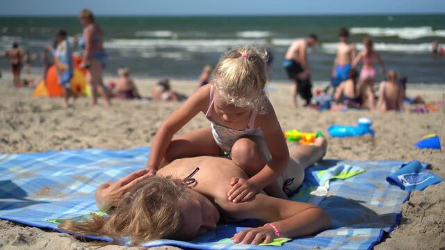 Girl sitting and massaging mother back on beach. Funny daughter do mom massage