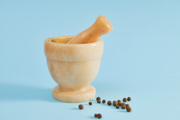 Marble beige mortar with pestle for grinding ingredients in cooking. Peppercorns lying on a blue...