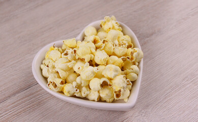 Popcorn in a white plate in the shape of a heart on a wooden background