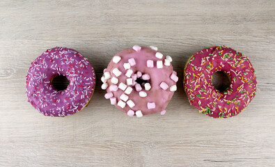 Round donuts on a wooden background. Round pink donuts with sprinkles and marshmallows