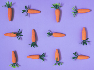 Artificial carrots lay down on pastel purple background pattern
