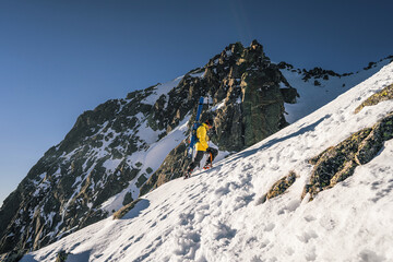 Side view of a male mountain climber going up snowy slope with axes against clouds. Ski tourer...