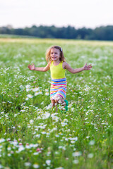 Naklejka na ściany i meble A little girl plays and runs in a flowery meadow