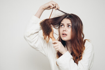 red-haired woman combing tangled curls on a light background