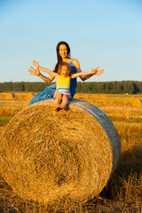 Naklejka na ściany i meble Little cute girl and her mom sitting on a bale of straw in a field