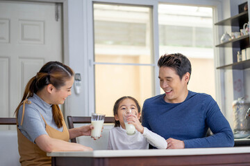 Asian family child girl and her father and mother drinking milk, having breakfast at kitchen. Happy family morning concept.