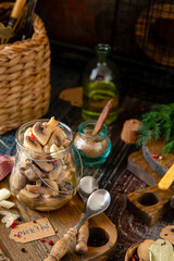 homemade marinated mushrooms in glass jar on wooden board with herbs, dill. pepper, vintage spoons