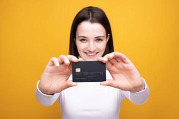 Close up portrait of young smiling business woman holding credit card, isolated on yellow background.