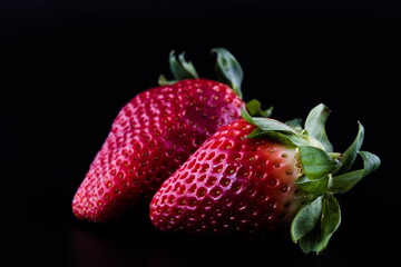 Two strawberries isolated on black background, close up