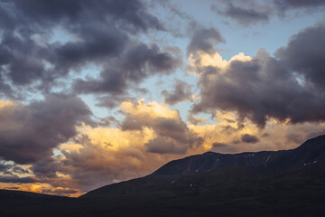 Beautiful mountain scenery with golden dawn light in cloudy sky. Scenic mountain landscape with illuminating color in sunset sky. Silhouettes of mountains on sunrise. Gold illuminating sunlight in sky
