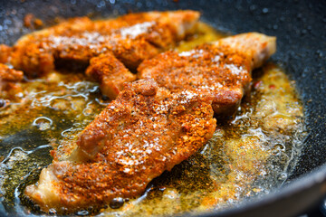 Large pieces of meat with spices are fried in a pan, close-up photo.