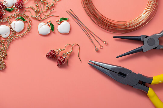 Making handmade jewelry at home. Production of earrings from metal accessories, wire and enamel pendants in the form of strawberries. Top view