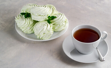 Handmade apple figured homemade marshmallow with mint on a white plate and tea in a white cup on a concrete table.