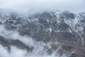 Epic Winter landscape image of view from Side Pike towards Langdale pikes with low level clouds on mountain tops and moody mist swirling around