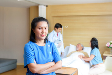 The nurse in the care of the patient smiles and folds her arms to look at a professional camera. Background picture of the patient in the hospital clinic..