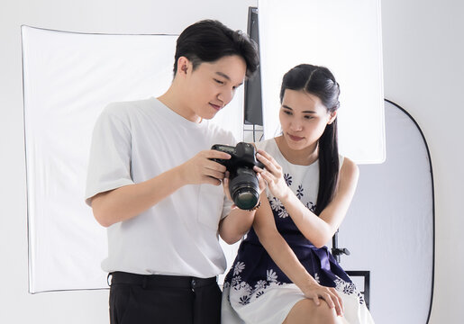Asian man photographer lets models view pictures taken on camera dslr screen.  Photography and model smiling happy in the white room at the studio. Concept camera photograher picture.