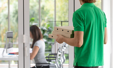 A young boy food delivery sender holding pizza paper boxes arrives at the customer's office and...