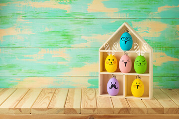 Easter holiday concept with colorful Easter eggs as cute bunny and chicken characters in toy house on wooden table