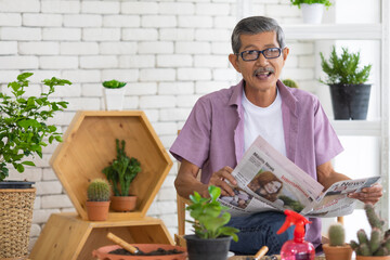 A senior Asian man sitting and drink coffee and reading the newspaper with happiness. Idea for relaxing and slowly life of older people after retirement
