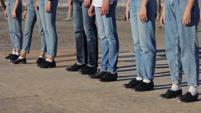 People in blue jeans and black shoes stand in one line. People are waiting for the command to take action.