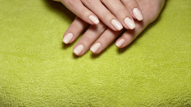 Result of doing professional manicure and naildesign in beauty nail salon. Pink shiny surface of healthy natural female nails after been manicured. 2 female hands isolated on green towel background