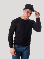 Young man tipping his hat, touching fedora hat on his head, in studio shot on white background