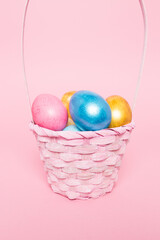Multi-colored Easter eggs in a basket on a pink isolated background. Easter is a bright holiday.