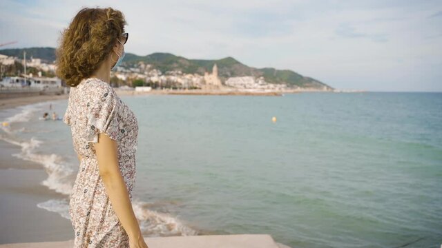 Beautiful curly brunette tourist looking at the Mediterranean village of Sitges during COVID-19. Safe Travel in the new normal.
