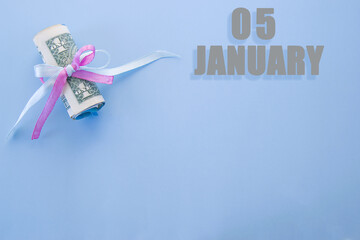 calendar date on blue background with rolled up dollar bills pinned by blue and pink ribbon with copy space. January 5 is the fifth day of the month