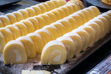 Roll cake sprinkled with powdered sugar cut into slices, lies on a dark plate.