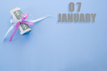 calendar date on blue background with rolled up dollar bills pinned by blue and pink ribbon with copy space. January 7 is the seventh day of the month