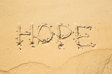 inscription Hope on the sand of the beach is washed by a soft wave. Top view.