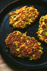Vegetable zucchini and carrot fritters on a frying pan and a wooden cutting board, close-up photo